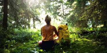 Rear view of woman hiker sitting on the ground outdoors in forest, resting.